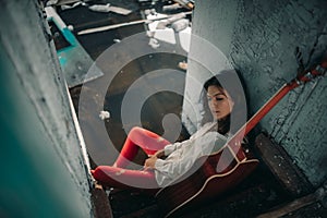 A young woman sits with guitar inside of old abandoned ship