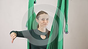 Young woman sits on a hammock smiling showing dislike sign. Aerial aero fly fitness trainer workout. Meditates, harmony