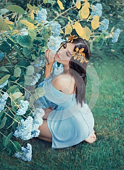 A young woman sits on her knees and hugs blooming blue hydrangeas