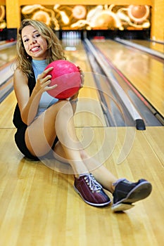 Young woman sits and holds ball in bowling club