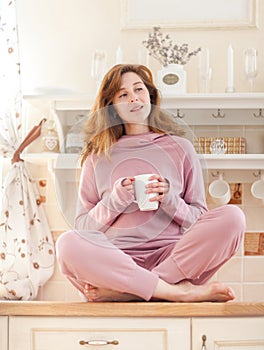 Young woman sits in the kitchen with cup of tea