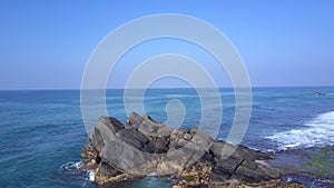 Young woman sits on large rocky cliff against endless ocean