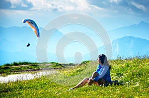Young woman sits in the meadow and looks at the paraplane.
