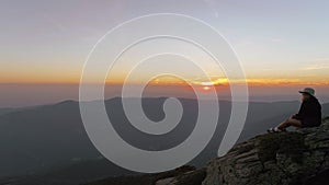 Young woman sits on mountain top or peak at sunset