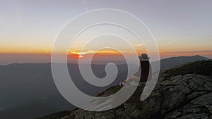 Young woman sits on mountain top or peak at sunset