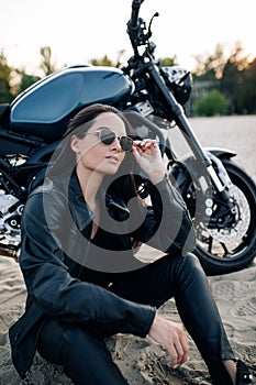 Young woman sits near black motorbike among beach