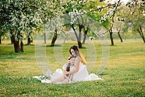 Young woman sits on a picnic blanket and hugs her daughter. mother and daughter`s summer picnic in the apple orchard