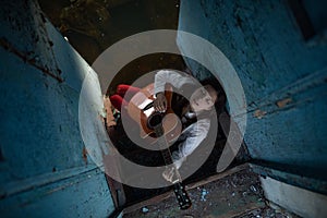 A young woman sits and plays guitar inside of old abandoned ship