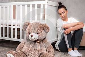 Young woman sits sad by the crib. Postpartum Depression Concept photo