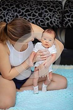 A young woman sits on a sofa at home and holds her little baby. Newborn child