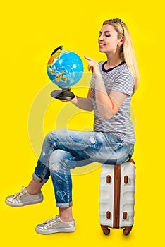 A young woman sits on a suitcase with a globe and is going on a journey.