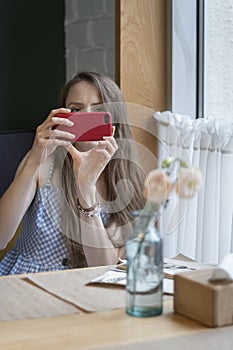 Young woman sits at table in cafe and takes selfie. Girl in coffee shop with phone in her hands. Vertical frame