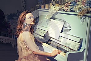 A young woman sits at a vintage piano. A pianist at a musical instrument decorated with candles and flowers