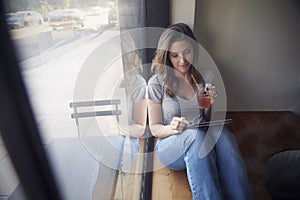 Young woman sits beside window in cafe using tablet computer