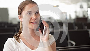 Young woman sitting in airport waiting room. Casual businesswoman talking on mobile with colleague