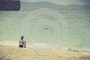 Young woman sitting alone on the beach looking at the sea and sky