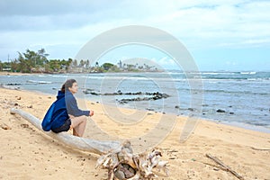 Young woman sitting alone on log by Hawaiian ocean