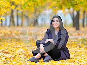 Young woman sitting amongst autumn leaves.