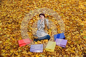 Young woman sitting on autumn leaves near colorful shopping bags. Autumn sale