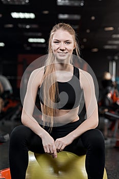 Young woman sitting with a ball in the gym