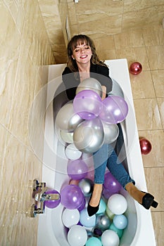 Young Woman Sitting in a Bathtub Full of Balloons in Bathroom Throwing Balloons in the Air
