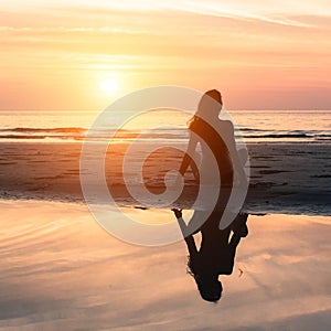 Young woman sitting on the beach during the amazing sunset