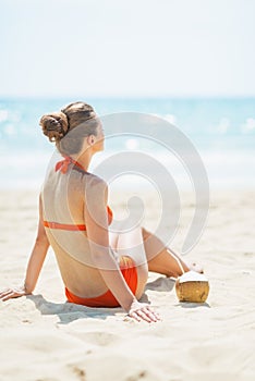 Young woman sitting on beach with coconut