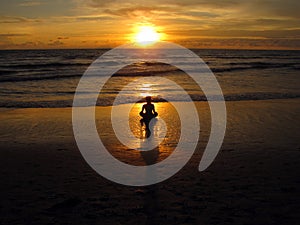 Young woman sitting on the beach, silhouette at sunset. Young woman practicing yoga outdoors. Harmony and meditation concept.