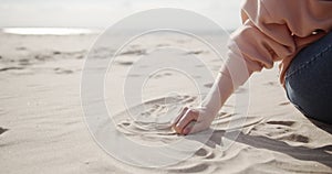 Young woman sitting on a beach stroking sand by hand passing it through fingers