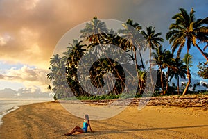 Young woman sitting on a beach at sunrise in Lavena village on Taveuni Island, Fiji