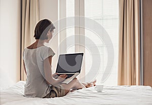 Young woman sitting on the bed at home and using laptop computer