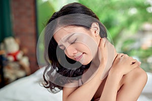 Young woman sitting on the bed with pain in neck