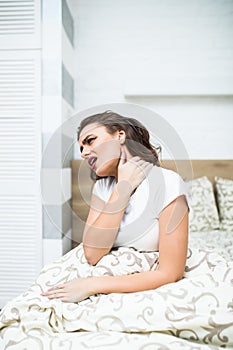 Young woman sitting on the bed with pain in neck at home