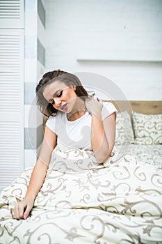 Young woman sitting on the bed with pain in neck at home