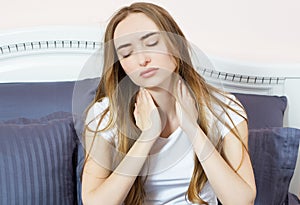 Young woman sitting on the bed with pain in neck in the morning