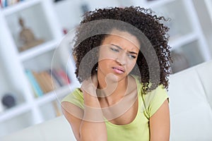 Young woman sitting on bed with pain in neck