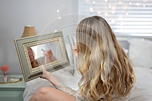 Young woman sitting on bed putting on makeup