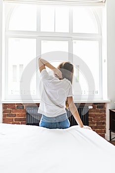 Young woman sitting in bed stretching and rubbing stiff back muscles after waking up in morning. Lady suffering from backache afte