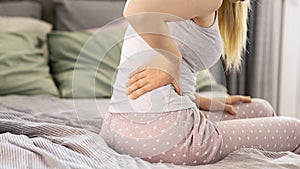Young woman sitting on bed and suffering from back pain