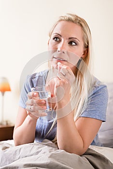 Young woman sitting in bed taking a tablet