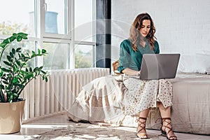 Young woman sitting on bed and using laptop in bedroom at home