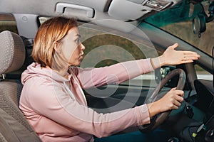 A young woman is sitting behind the wheel of a car points to the road with her hand. Side view, from inside the car