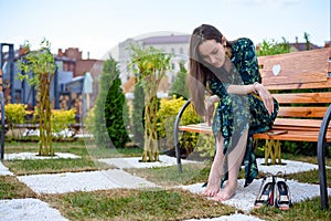 Young woman sitting on bench barefoot next to high heel shoes, rest from shoes