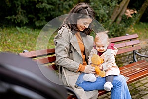 Young woman sitting on a bench with cute baby girl in the autumn park