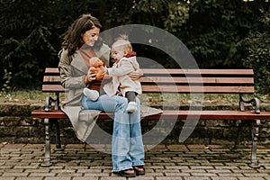 Young woman sitting on a bench with cute baby girl in the autumn park