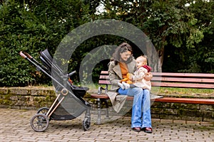 Young woman sitting on a bench with cute baby girl in the autumn park