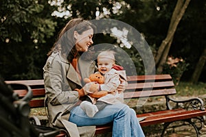 Young woman sitting on a bench with cute baby girl in the autumn park