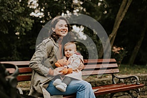 Young woman sitting on a bench with cute baby girl in the autumn park