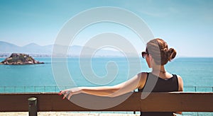 Young woman sitting on a bench and looking at the sea