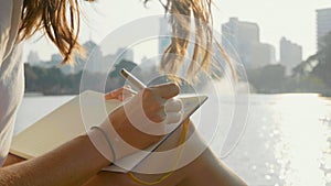 Young woman sitting on the bench in park and writing in diary, close-up